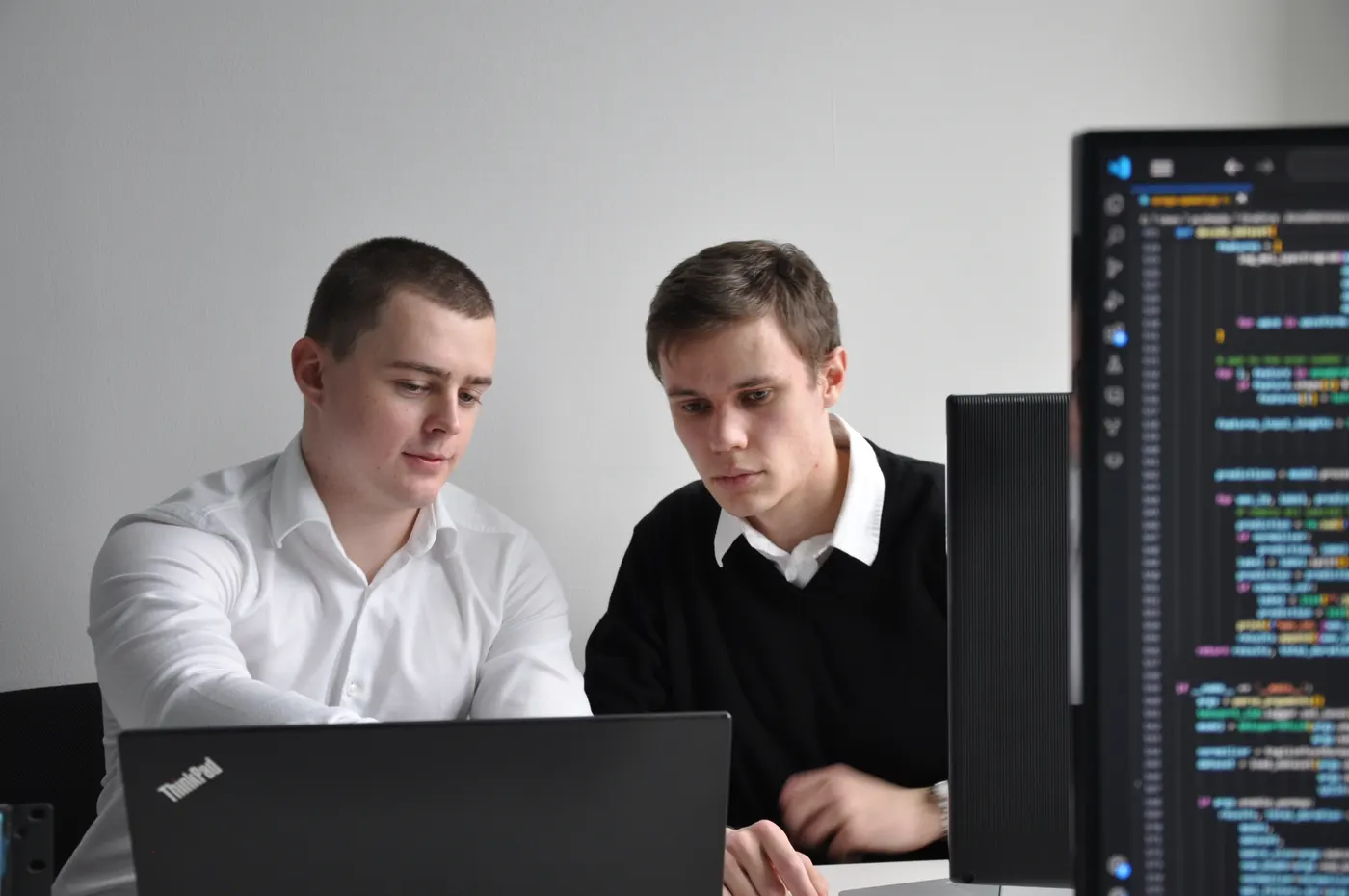 Two Ollsoft engineers at a laptop, code on a monitor beside them